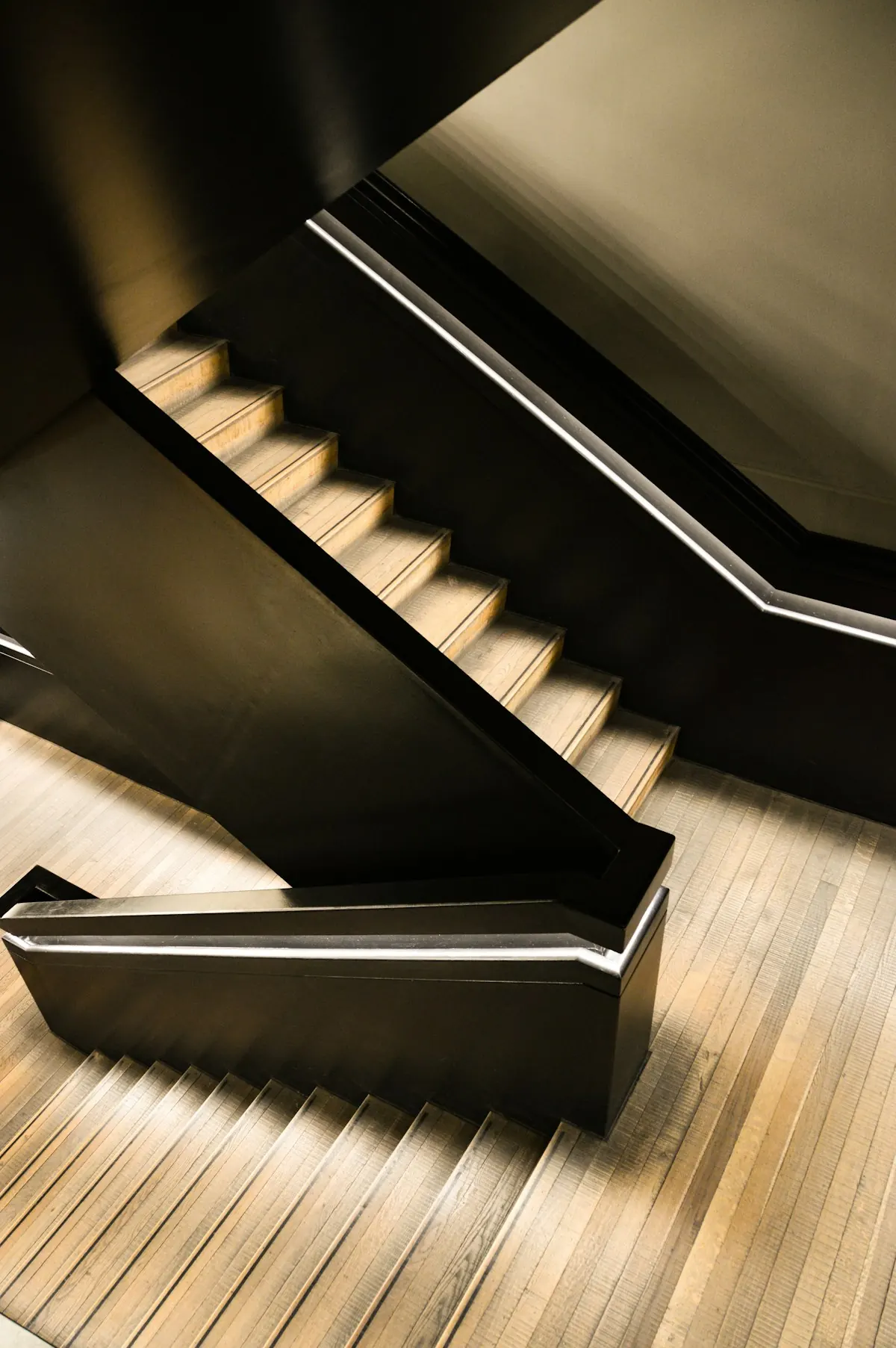 Escalier deux quartiers tournants en chêne massif, vu en plongée, marches éclairées dans la pénombre.