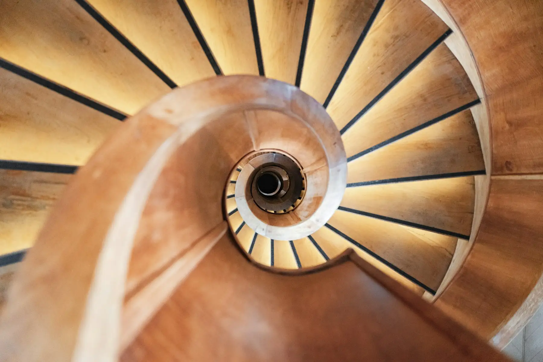 Escalier hélicoïdal en bois massif vu depuis le palier haut, les marches rayonnent en éventail autour du noyau central.
